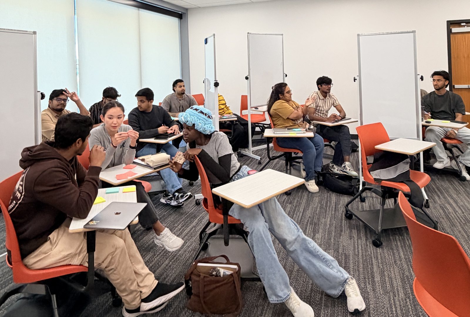 Students at San Francisco Bay University working in small groups on rolling chairs, with sticky notes, laptops and mobile whiteboards